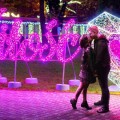 Para stojąca przy podświetlanym napisie „Miłość” LED neon oraz sercu 3D LED podczas wieczornej iluminacji miejskiej, dekoracja walentynkowa w przestrzeni publicznej.