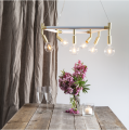 Lampa wisząca z kilkoma żarówkami LED nad drewnianym stołem z kwiatami i świecą. Ciepłe światło tworzy elegancką, przytulną atmosferę wnętrza.