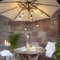 Girlanda LED z przezroczystymi żarówkami zamontowana na parasolu ogrodowym nad stołem, tworząca nastrojowe oświetlenie tarasu.