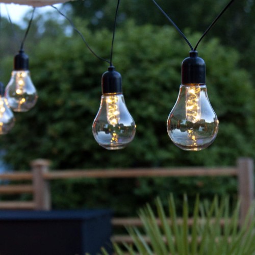 Girlanda ogrodowa LED GLOW z przezroczystymi kloszami i ciepłym białym światłem, zawieszona nad tarasem, z widocznymi żarówkami filamentowymi na czarnym przewodzie.