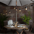 Girlanda świetlna 24V z żarówkami LED Filament G45 zawieszona nad stołem ogrodowym na tarasie. Ciepłe światło tworzy przytulną atmosferę w aranżacji z parasolem, drewnianymi meblami i dekoracjami stołu.