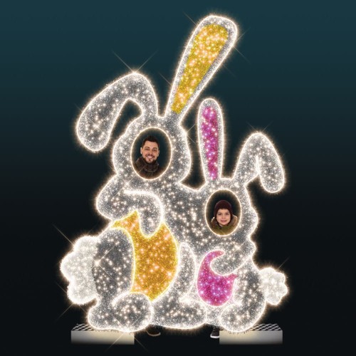 Iluminacja wielkanocna LED przedstawiająca dwa zające 2D z otworami do zdjęć, dekoracja świetlna do przestrzeni miejskich z kolorowymi elementami i gęstą siatką punktów LED.