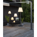 Lampa KRETA z wysokim czarnym metalowym słupkiem, okrągłą podstawą i białym rozszerzającym się ku dołowi kloszem.