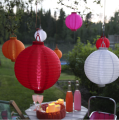 Kolorowe lampiony solarne LED zawieszone w ogrodzie nad stolikiem. Na pierwszym planie czerwony lampion, obok biały model tworzący klimatyczną dekorację przestrzeni wypoczynkowej.