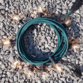 Girlanda ogrodowa z zielonym przewodem i żarówkami G45 LED 1,5W 2100K Soft Glow, ułożona w krąg na tle jasnych kamieni. Żarówki świecą ciepłym światłem, osadzone w czarnych oprawkach.