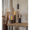 Minimalistyczna lampa TUB z wysoką czarną podstawą w kształcie cylindra i dekoracyjną żarówką.
