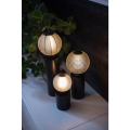 Minimalistyczna lampa TUB z wysoką czarną podstawą w kształcie cylindra i dekoracyjną żarówką.