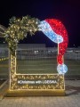 Świąteczna dekoracja LED w formie ramki z czapką Mikołaja i ośnieżonym igliwiem, ustawiona na zewnątrz przy ogrodzeniu, z napisem „#Christmas with LGESWA”.