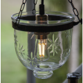 Szklana lampa wisząca z dekoracyjną żarówką LED E14 ST35 emitującą ciepłe światło w ogrodowej aranżacji.