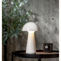 Biała lampa stołowa LED MUSHROOM świecąca na drewnianym stoliku, minimalistyczna aranżacja na tle betonowej ściany.