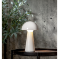 Biała lampa stołowa LED MUSHROOM świecąca na drewnianym stoliku, minimalistyczna aranżacja na tle betonowej ściany.