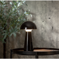 Świecąca lampa stołowa LED MUSHROOM na drewnianym stoliku, czarna obudowa i charakterystyczny kopułowy klosz.