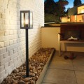 Lampa ogrodowa stojąca ALAMONTE 1 z wysokim czarnym słupkiem i prostokątną, przeszkloną oprawą.