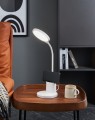 Na drewnianym stoliku lampa LED BROLINI doświetla przestrzeń pod płaską głowicą, wyróżniając się białą, minimalistyczną konstrukcją.