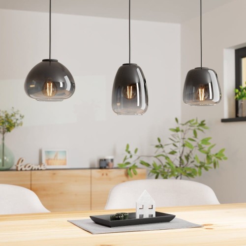 Lampa wisząca AGUILARES z trzema szklanymi kloszami w czarno-szaro-transparentnym wykończeniu, zawieszona nad stołem w jasnej jadalni.