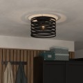 Czarna lampa sufitowa CREMELLA z ażurowym metalowym kloszem, zamontowana na suficie i emitująca światło przez poziome szczeliny.