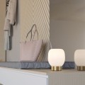 Lampa stołowa MANZANARES z białym szklanym kloszem i podstawą w kolorze szczotkowanego mosiądzu, ustawiona na komodzie w jasnym wnętrzu.