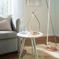 Lampa stołowa LED PALOZZA 8,8W o smukłej metalowej konstrukcji w kolorze różowego złota, ustawiona na stoliku i emitująca ciepłe białe światło 3000K.