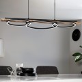 Lampa wisząca LED BOYAL z podłużnym drewnianym elementem i trzema świetlnymi pierścieniami, zawieszona nad wyspą kuchenną i emitująca ciepłe białe światło 3000K.