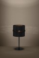 Włączona lampa stołowa PARAGUAIO tworzy ciepłą poświatę, podkreślając czarny cylindryczny klosz i minimalistyczną podstawę.