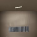 Lampa wisząca TAMARESCO z podłużnym szarym aksamitnym kloszem, zawieszona na jasnych przewodach i emitująca delikatne światło na ścianę.