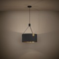Lampa wisząca TORTOLA 1 z czarnym cylindrycznym kloszem z tkaniny i mosiężnymi detalami, zawieszona na tle ciemnej ściany i emitująca ciepłe światło.