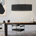 Lampa wisząca MARASALES z podłużnym czarnym kloszem z tkaniny, ozdobionym geometrycznym wzorem w kolorze mosiądzu, zawieszona nad stołem.