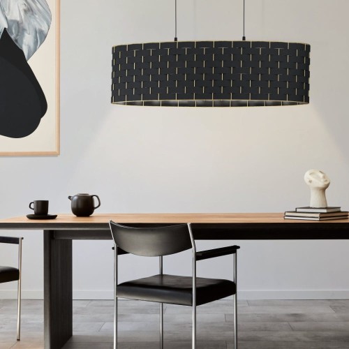 Lampa wisząca MARASALES z podłużnym czarnym kloszem z tkaniny, ozdobionym geometrycznym wzorem w kolorze mosiądzu, zawieszona nad stołem.
