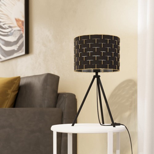 Lampa stołowa MARASALES z czarnym cylindrycznym abażurem ozdobionym geometrycznym wzorem w kolorze mosiądzu, ustawiona na trójnożnej podstawie.