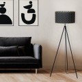 Lampa podłogowa MARASALES z czarnym cylindrycznym abażurem i trójnożną metalową podstawą, ustawiona obok sofy w nowoczesnym salonie.