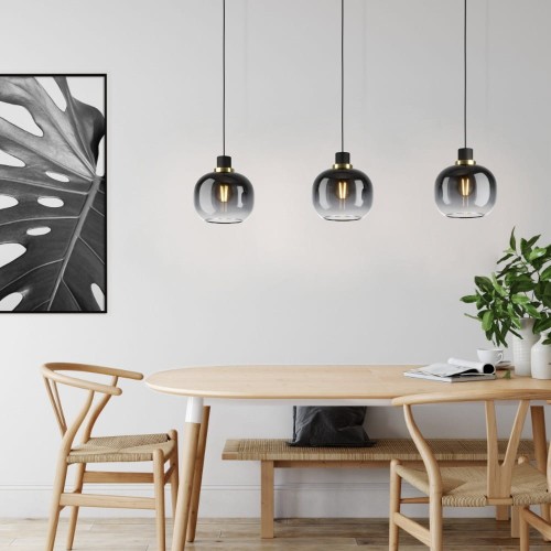 Lampa wisząca OILELLA z trzema kulistymi kloszami z przyciemnianego szkła w czarno-szarym odcieniu, zawieszona nad drewnianym stołem w jasnej jadalni.