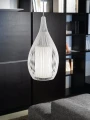 Lampa wisząca RAZONI z białym kloszem w kształcie kropli, zawieszona na tle ciemnych mebli, z widoczną ażurową strukturą metalowych drutów.