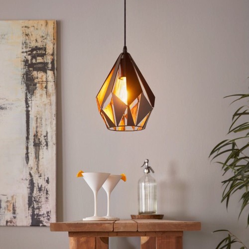 Lampa wisząca CARLTON 1 z geometrycznym kloszem z czarnych metalowych pasów i miedzianym wnętrzem, zawieszona nad stołem w jasnym pomieszczeniu.