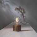 Żarówka LED E27 G125 na drewnianej podstawie, włączony filament i delikatne światło w nastrojowej aranżacji.