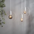 Nowoczesne lampy wiszące z dekoracyjnymi żarówkami LED w metalowych oprawach na tle jasnej ściany z rośliną pnącą.