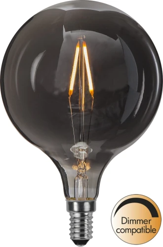 Żarówka LED E14 G95 dymiona z filamentami świecącymi ciepłym światłem na białym tle. Dekoracyjne źródło światła kompatybilne ze ściemniaczem.