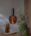 Dekoracyjna żarówka LED filament z bursztynowego szkła zawieszona nad drewnianym stołem obok rośliny doniczkowej i szklanych butelek. Designerskie oświetlenie emitujące ciepłe światło dekoracyjne.