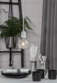 Wisząca lampa z dekoracyjną żarówką LED o kulistej bańce z fakturą szkła nad stołem z naczyniami w jasnym wnętrzu.