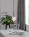 Wisząca lampa z dekoracyjną żarówką LED o kulistej bańce z fakturą szkła nad stołem z kieliszkami i rośliną w doniczce.