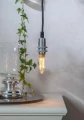 Żarówka LED filament E14 w metalowej oprawie wiszącej, ciepłe światło na tle jasnej ściany.