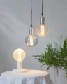 Dekoracyjne lampy z żarówkami LED filament G125 w oprawach wiszących oraz lampie stołowej w jasnym wnętrzu.