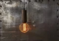 Wisząca lampa z dekoracyjną żarówką LED w złotej metalowej klatce na tle industrialnej ściany metalowej.