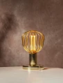 Lampa stołowa z dekoracyjną żarówką LED w złotej metalowej klatce ustawiona na jasnym blacie na tle ściany w ciepłej aranżacji wnętrza.