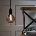 Wisząca lampa z dekoracyjną żarówką LED filament w przydymionej ryflowanej bańce nad drewnianym krzesłem z książkami.