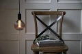Wiszące lampy z dekoracyjnymi żarówkami LED filament w różnych kształtach kloszy nad drewnianym stołem i krzesłami.