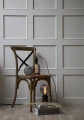 Wisząca lampa z dekoracyjną żarówką LED filament nad drewnianym krzesłem z książkami w minimalistycznej aranżacji wnętrza.
