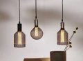 Dekoracyjna lampa stołowa z żarówką LED filament ustawiona na krześle oraz druga lampa na podłodze obok książek.