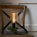 Lampa stołowa z dekoracyjną żarówką LED filament w ryflowanej bursztynowej bańce ustawiona na książkach na drewnianym krześle.