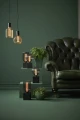Dekoracyjne lampy z żarówkami LED filament ustawione na zielonych podestach obok skórzanego fotela w eleganckim wnętrzu.