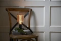 Lampa stołowa z dekoracyjną żarówką LED filament w ryflowanej bursztynowej bańce ustawiona na krześle w jasnym wnętrzu.